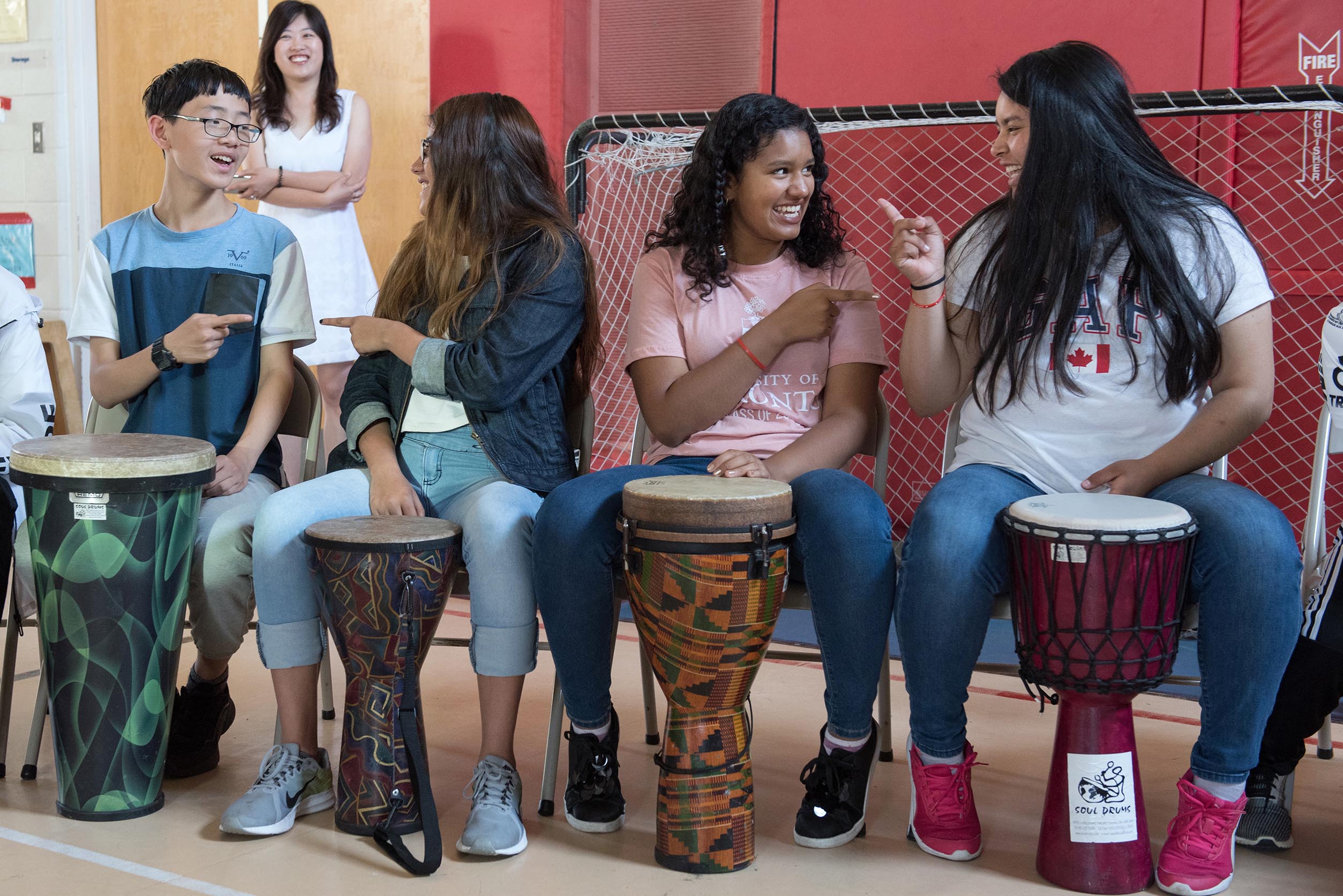 Students sitting side by side playing the drums Open Gallery